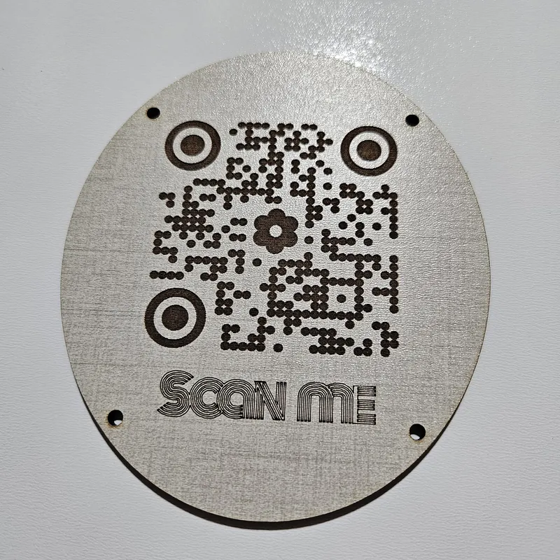 QR code sign laser-engraved on TruFlat Linen plywood with dot pattern styling, flower center logo, and Scan Me label